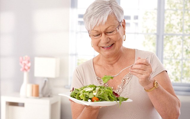 An older woman enjoying a salad while wearing dentures