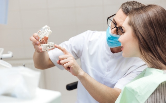 Dentist using model smile to explain the four step dental implant process