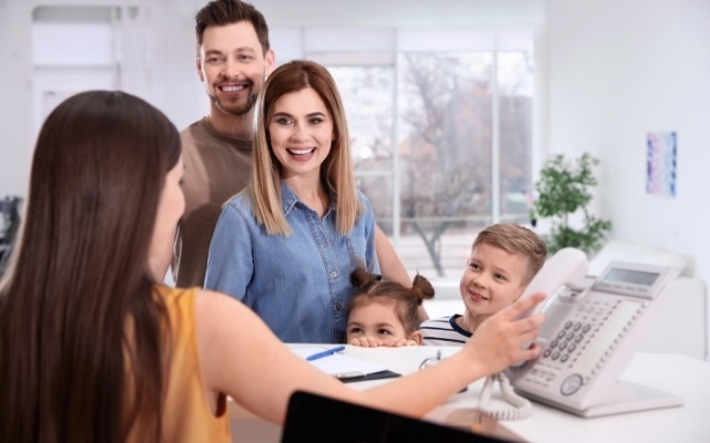 Family filling out dental insurance forms at dental office front desk