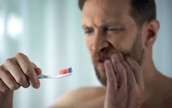 Man holding his mouth and looking at toothbrush