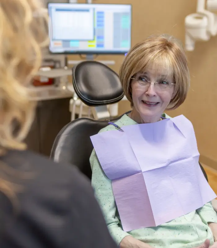 Woman with glasses talking to her dentist while in the dental chair