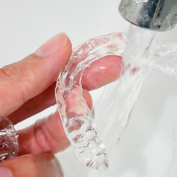 A person cleaning their Invisalign aligners with water 