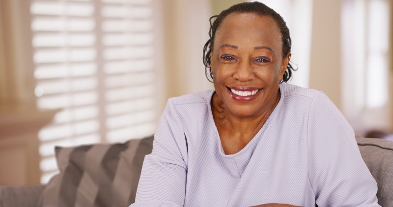 an older woman wearing a lavender blouse and smiling after receiving her implant-retained dentures in Chaska