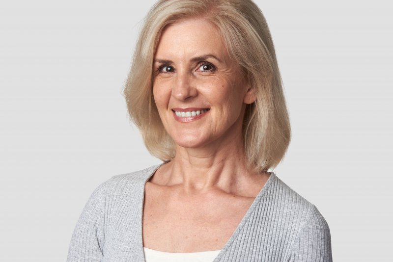 an older woman wearing a gray blouse and smiling after receiving her dental implants