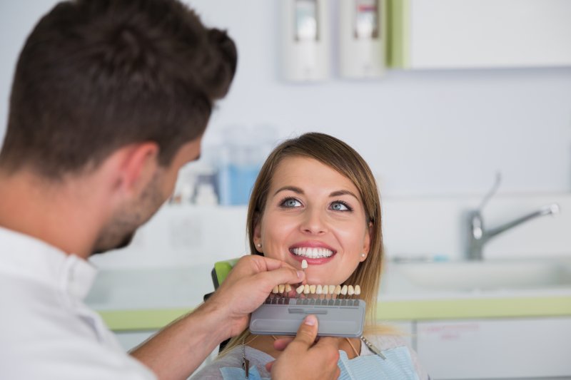 a dentist using a shade guide to determine the color of a patient’s veneers