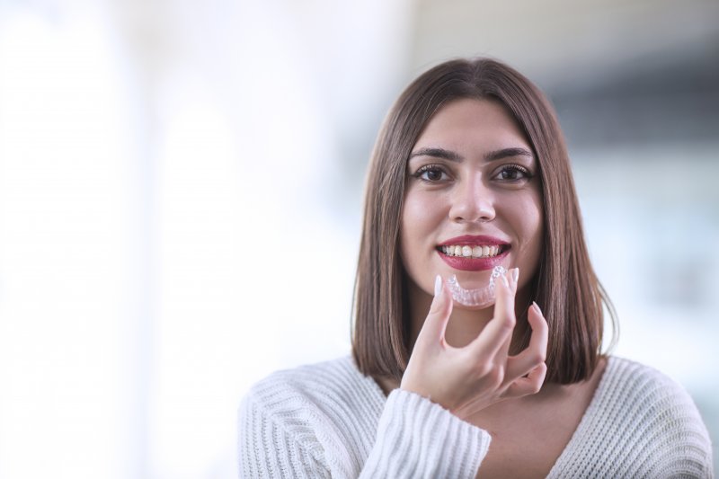 a woman holding an Invisalign aligner and preparing to insert it into her mouth while smiling