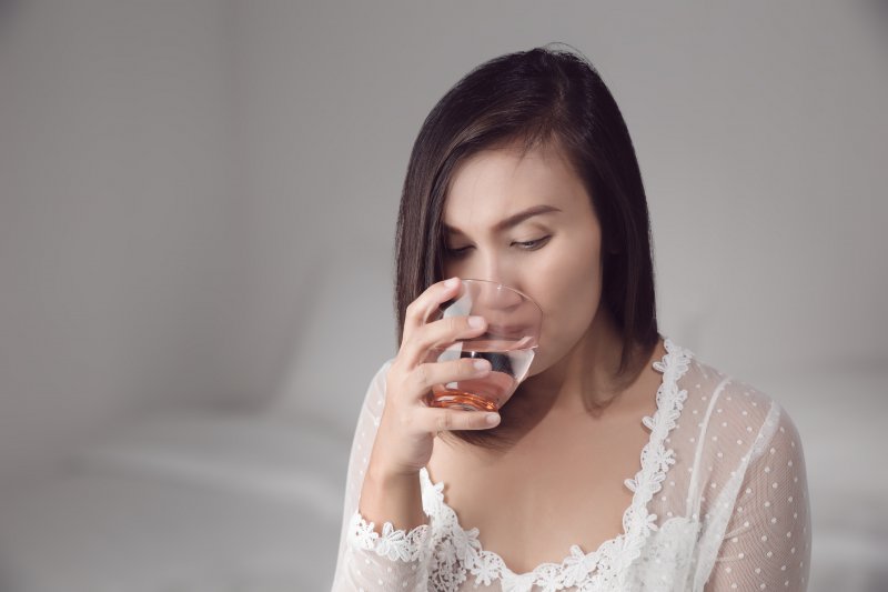 a young woman sipping a glass of water to treat her dry mouth